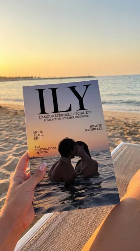 Magazine photo de couple personnalisé intitulé ILY, tenu à la main face à un coucher de soleil sur la plage